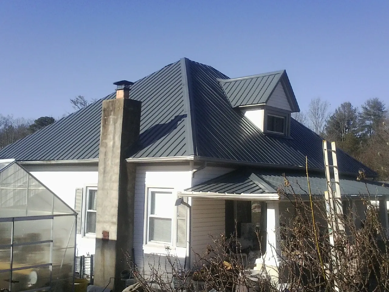 Dark blue standing seam metal roof on a white farmhouse with dormer — Slate & Tile Roof Repair by Roofing Brothers in West Columbia