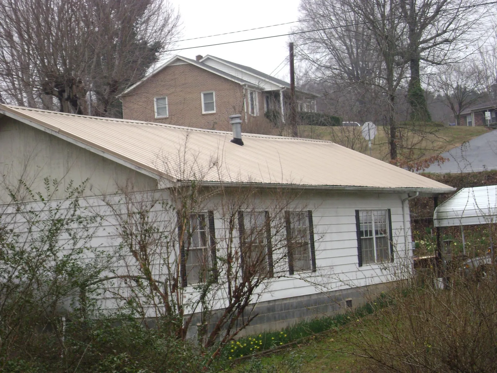 Tan metal roof on a white sided house set into a hillside — Commercial Roofing by Roofing Brothers in West Columbia